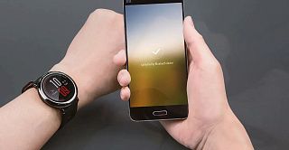 Круглые часы на руке и смартфон с сообщением о разблокировке по Bluetooth