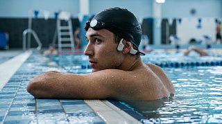 Пловец у бортика бассейна в костных наушниках Shokz OpenSwim Pro под силиконовой шапочкой