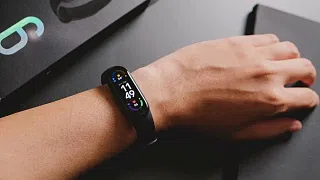 Фитнес-браслет Xiaomi на руке рядом с фирменной коробкой, на экране 11:49