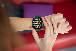 Часы Apple Watch с зелёным ремешком на руке, на экране сетка иконок приложений