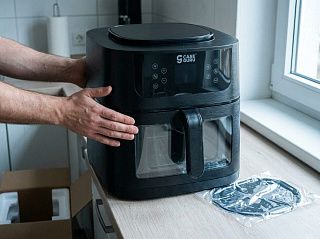 Распакованный аэрогриль Жароваров ставят на столешницу, рядом стоит открытая коробка и плёнка