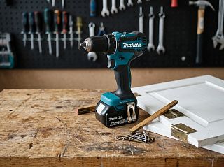 Дрель-шуруповерт Makita DDF485RFE с батареей 3,0 А·ч на верстаке рядом со снятой дверцей шкафа