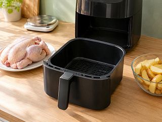 Пустая выдвижная чаша аэрогриля между целой сырой курицей на тарелке и миской нарезанного картофеля