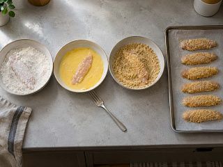 Панировка куриных полосок по шагам: мука, яично-молочная смесь, сухари и готовые полоски на подносе