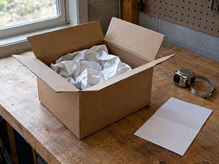 Картонная коробка с упаковочной бумагой на верстаке в гараже: проверка при получении